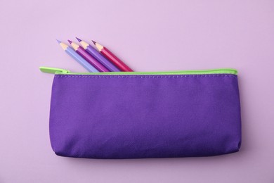 Many colorful pencils in pencil case on pink background, top view