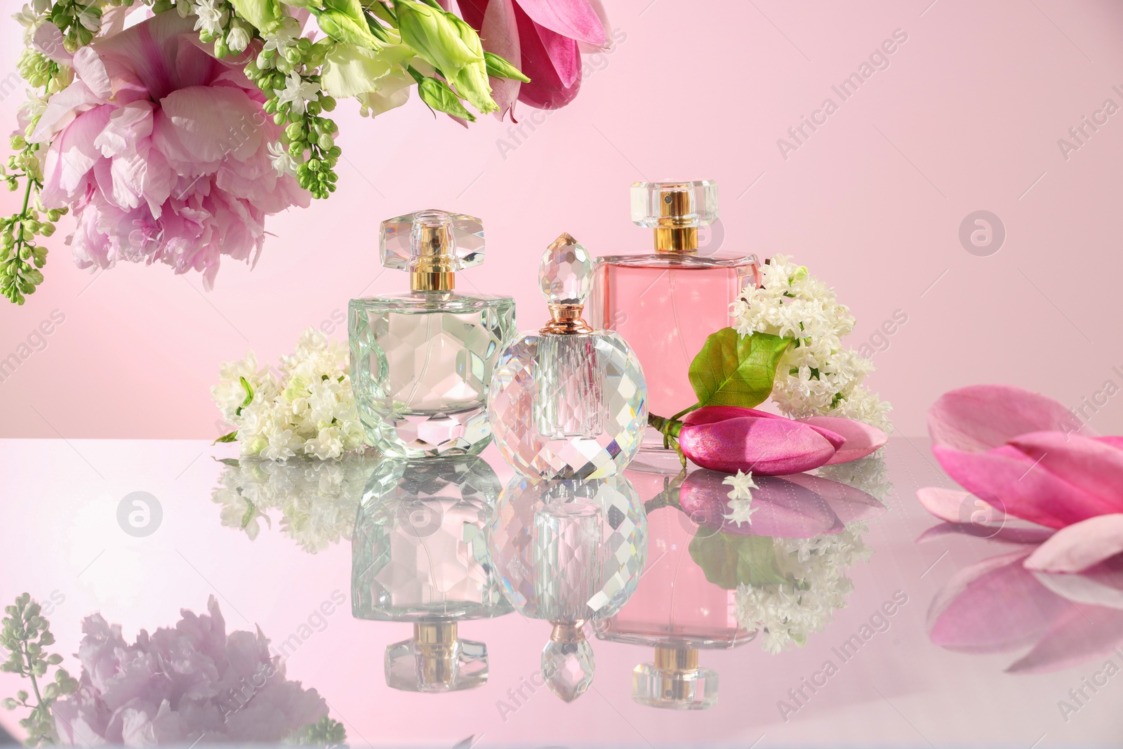 Photo of Luxury perfumes and floral decor on mirror surface against pink background