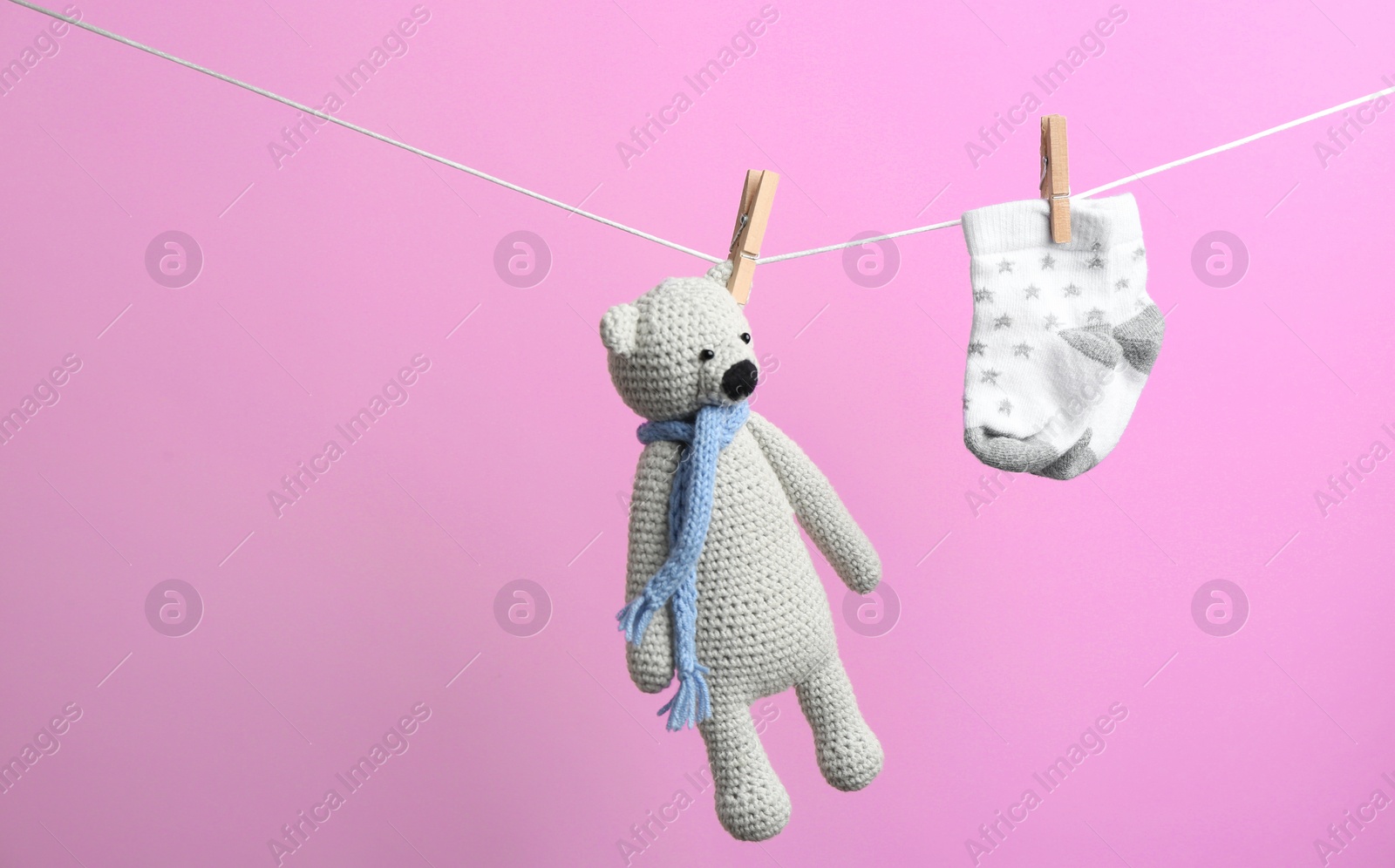 Photo of Small socks and toy bear hanging on washing line against color background, space for text. Baby accessories