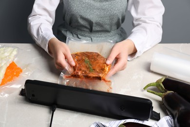 Photo of Woman using sealer for vacuum packing on white marble table, closeup