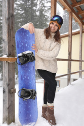 Photo of Young woman with snowboard wearing winter sport clothes and goggles outdoors