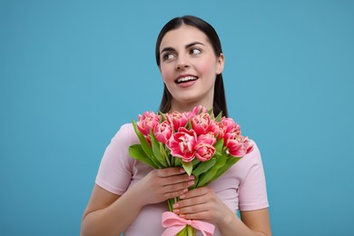 Happy young woman with beautiful bouquet on light blue background