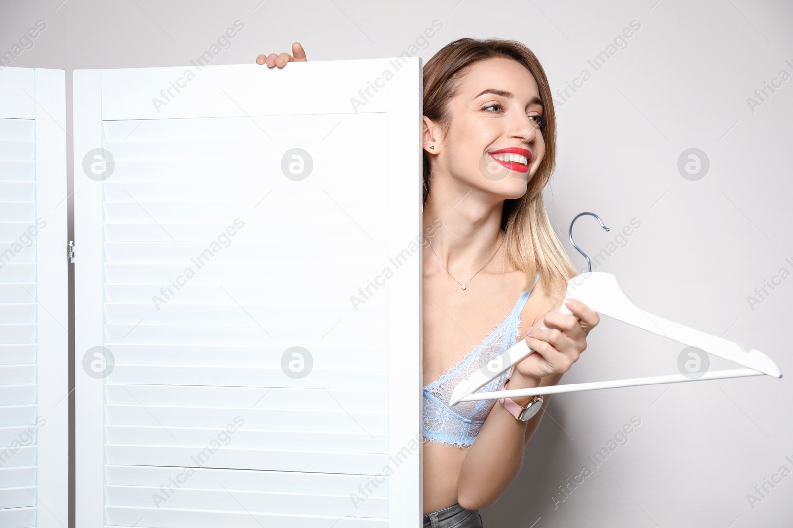 Photo of Young woman with hanger behind folding screen against light background. dressing room