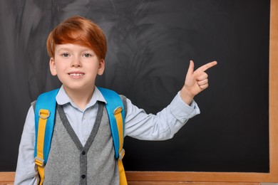 Smiling schoolboy pointing at something near blackboard