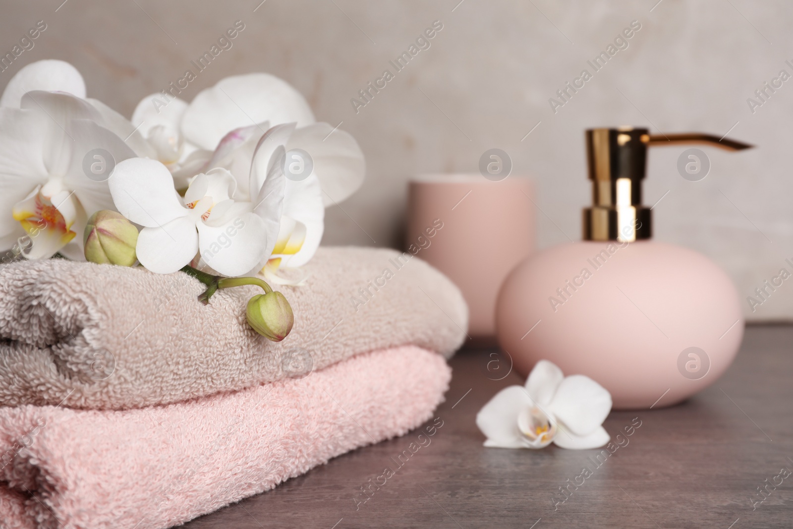 Photo of Stylish soap dispenser and towels with flowers on table