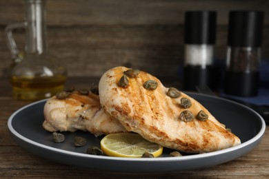 Photo of Delicious chicken fillets with capers and lemon served on wooden table, closeup