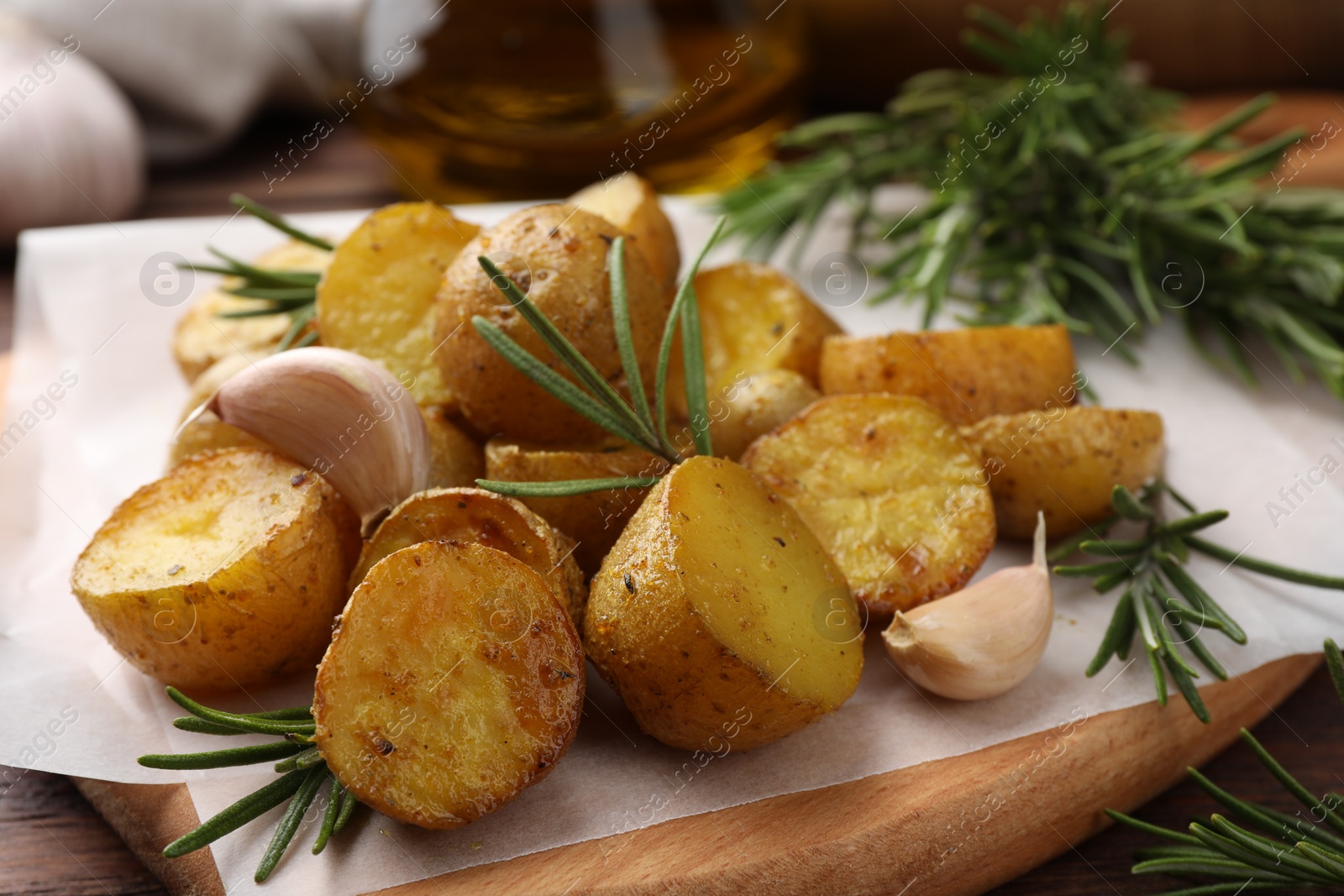 Photo of Delicious baked potatoes with rosemary and garlic on parchment paper, closeup