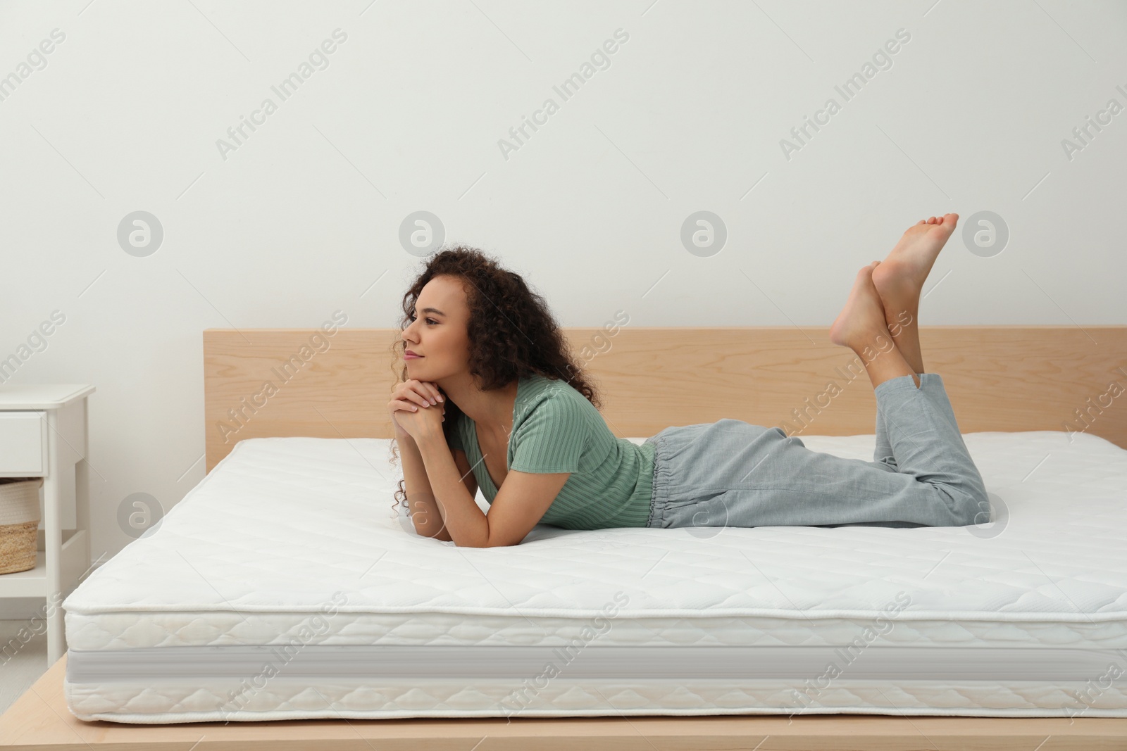 Photo of Happy young African American woman on bed with comfortable mattress at home