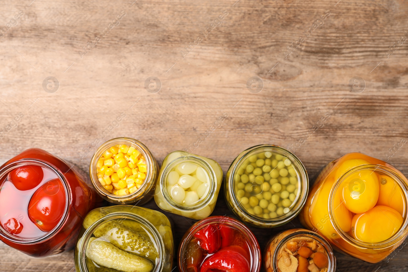 Photo of Glass jars with different pickled vegetables on wooden table, flat lay. Space for text