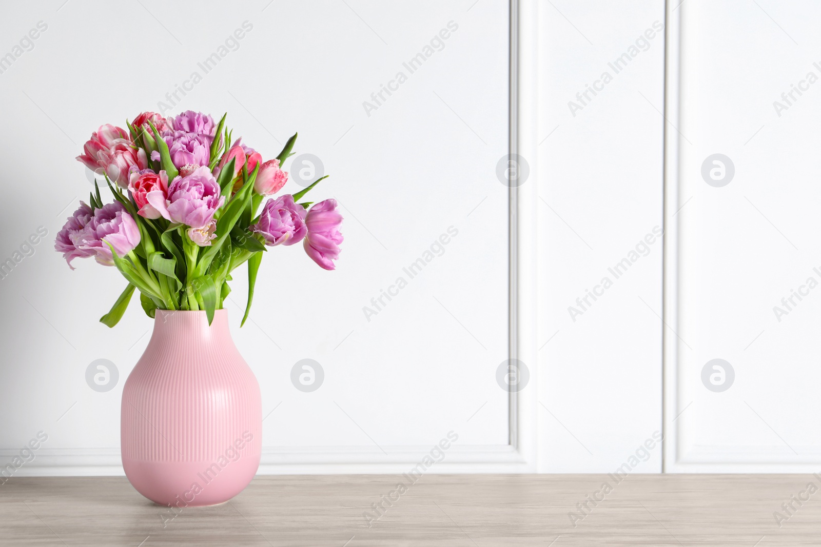 Photo of Beautiful bouquet of colorful tulip flowers on floor near white wall, space for text