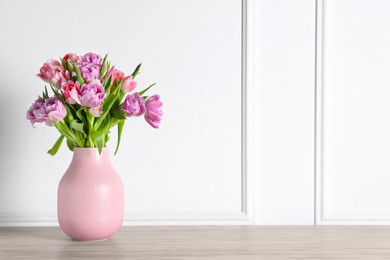 Photo of Beautiful bouquet of colorful tulip flowers on floor near white wall, space for text