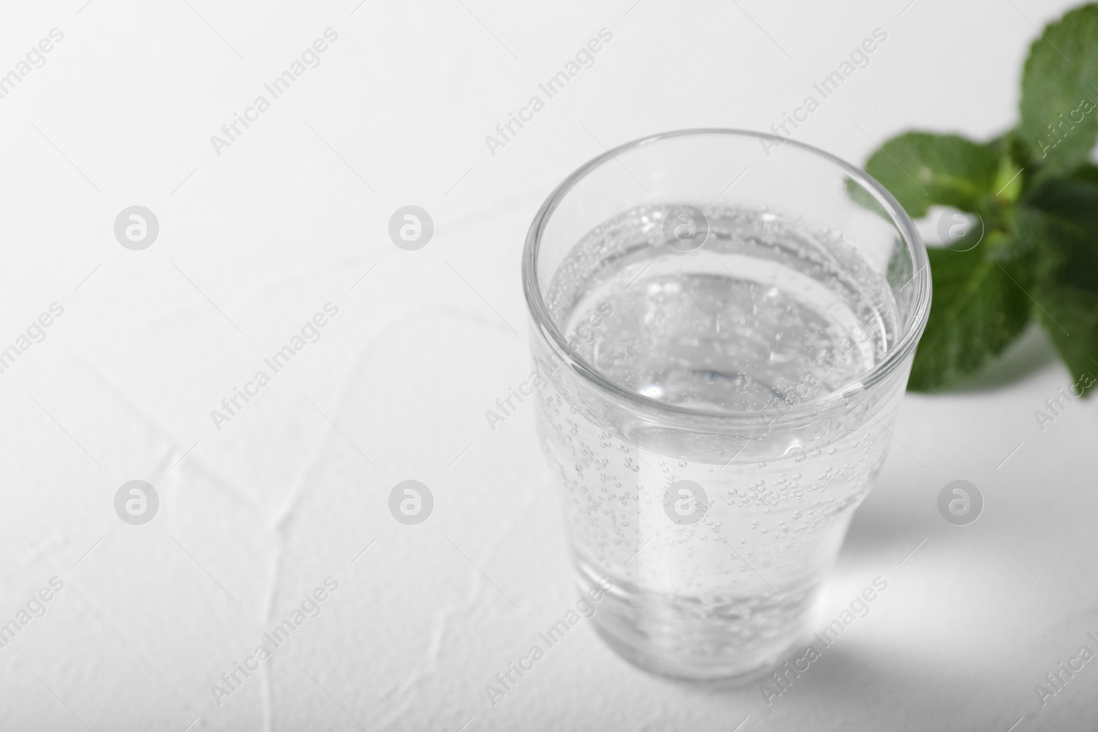 Photo of Glass of soda water on white table, closeup. Space for text