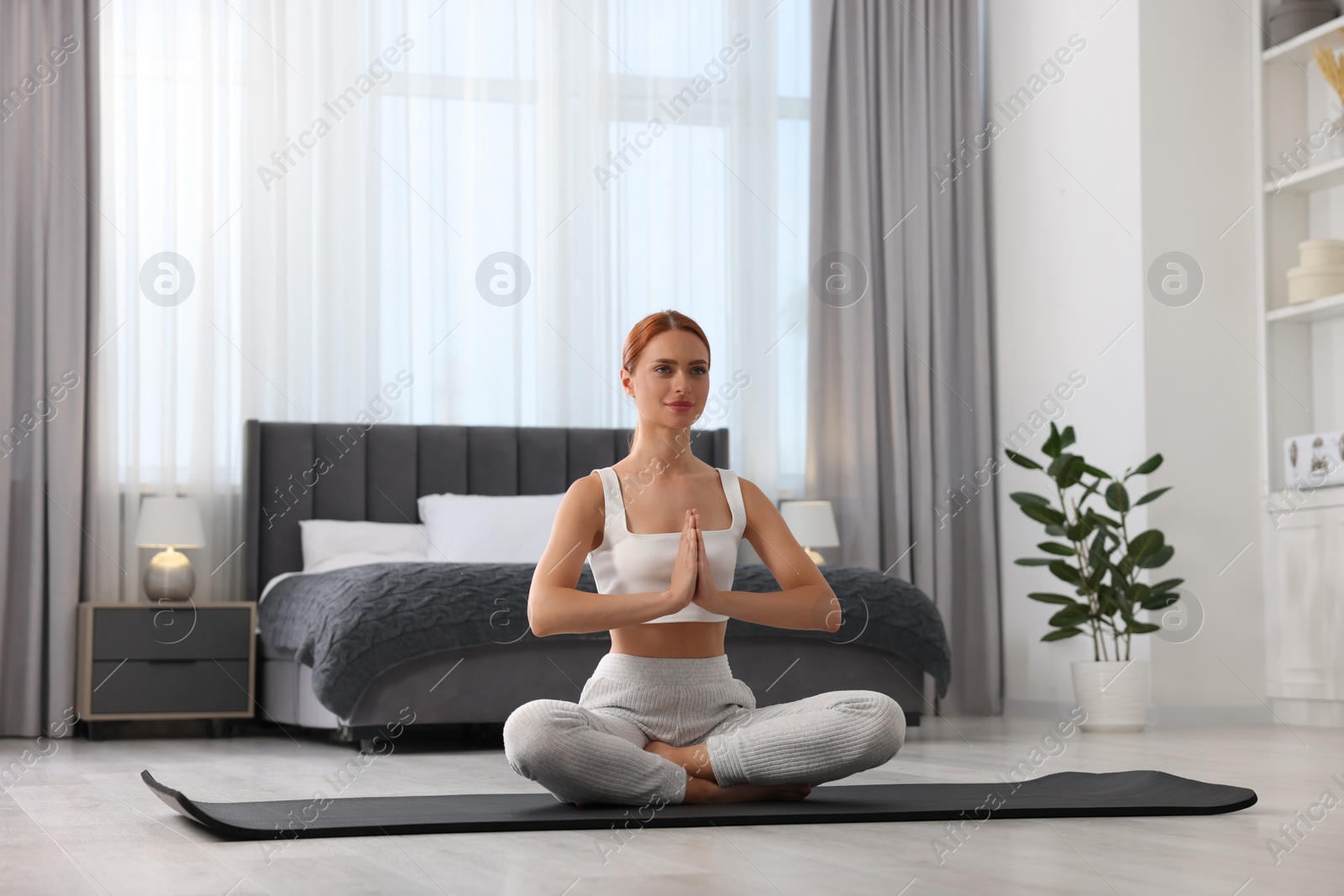 Photo of Beautiful young woman practicing Padmasana on yoga mat at home. Lotus pose