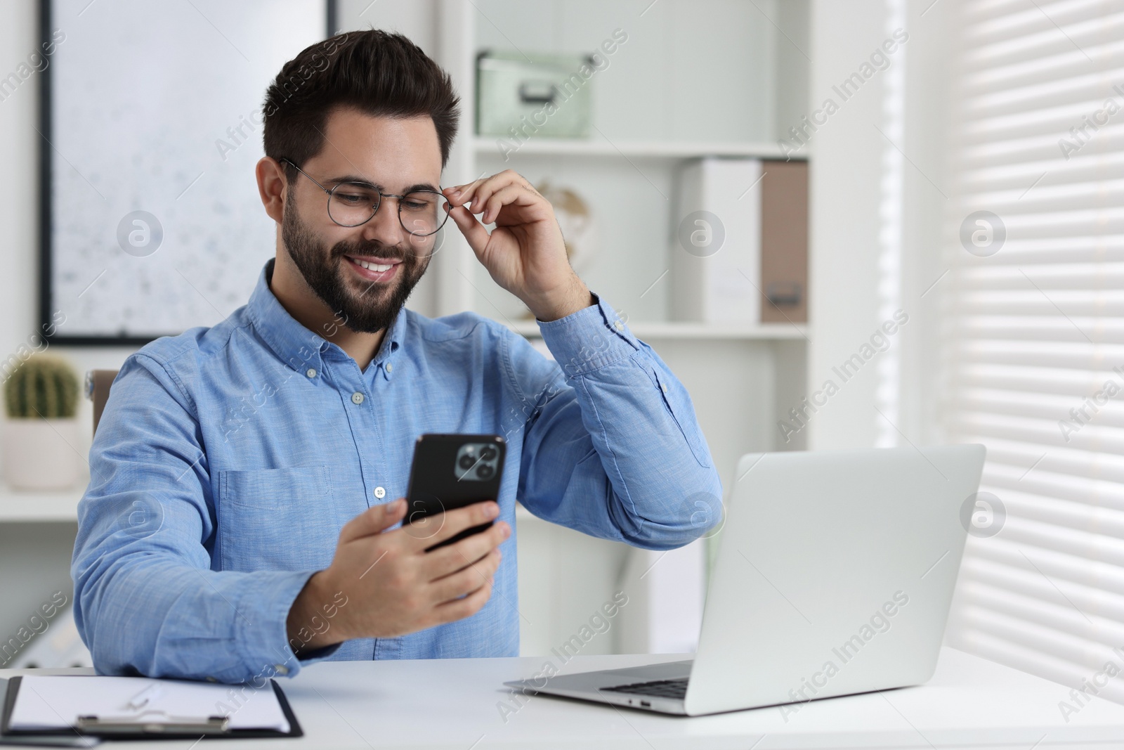 Photo of Happy young man using smartphone at white table in office