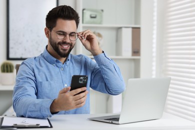 Happy young man using smartphone at white table in office