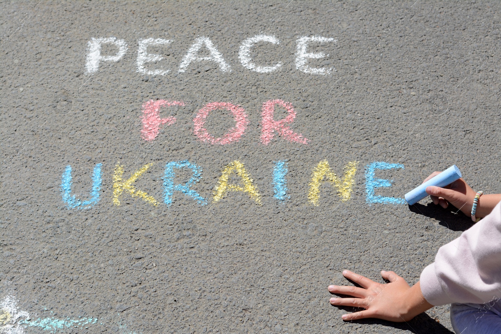 Photo of Girl writing Peace For Ukraine with colorful chalks on asphalt outdoors, closeup