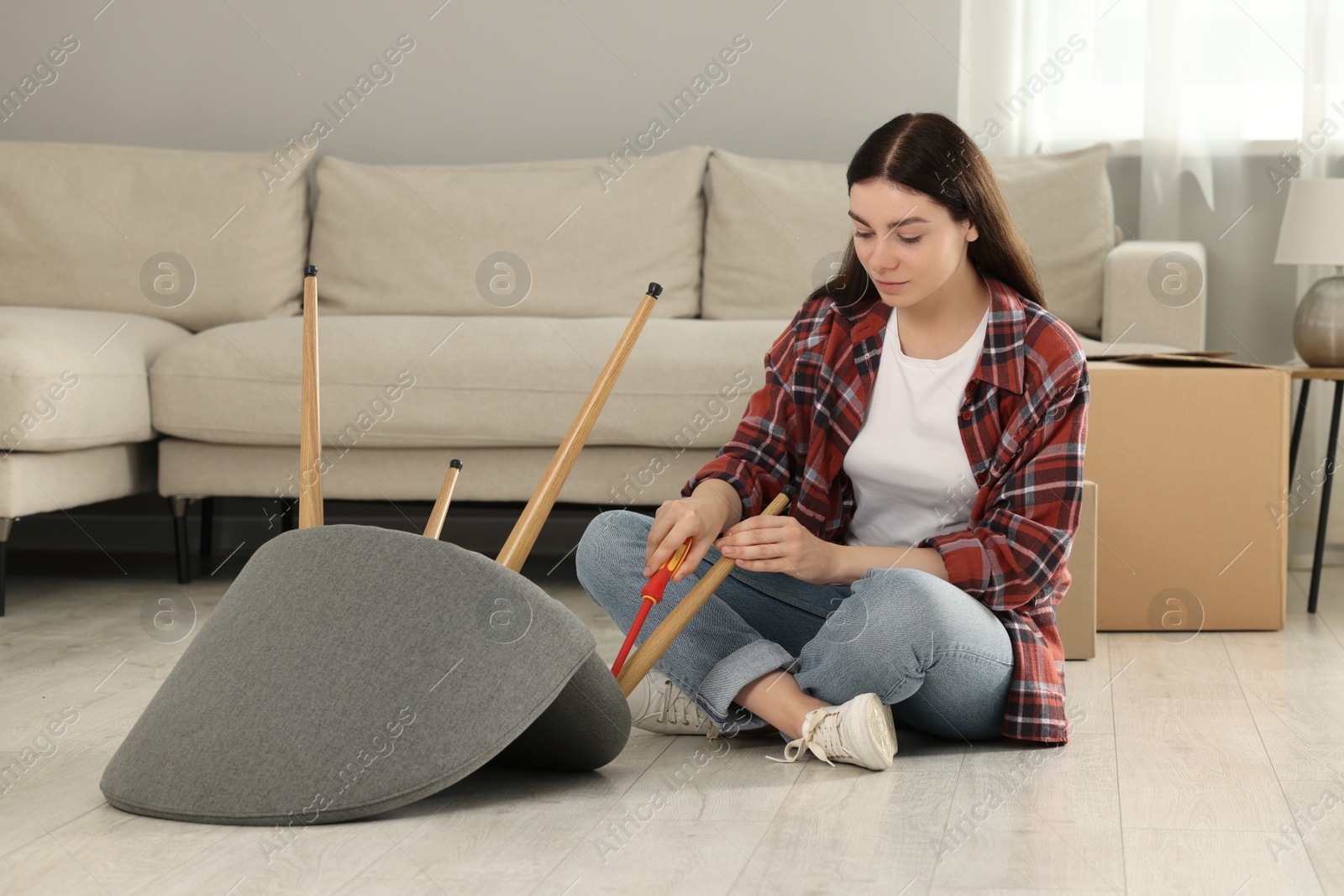 Photo of Young woman with screwdriver assembling armchair on floor at home