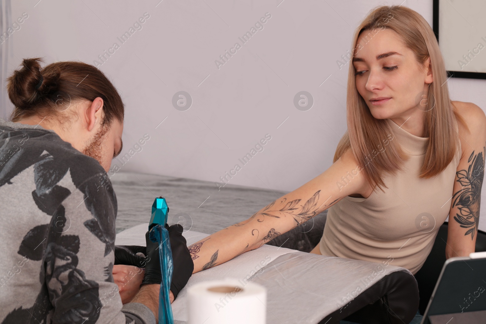 Photo of Professional artist making tattoo on arm in salon