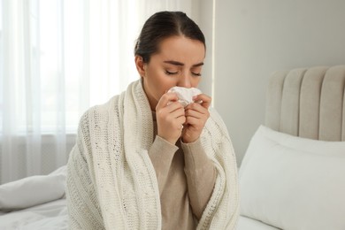 Sick young woman with tissue wrapped in knitted plaid at home