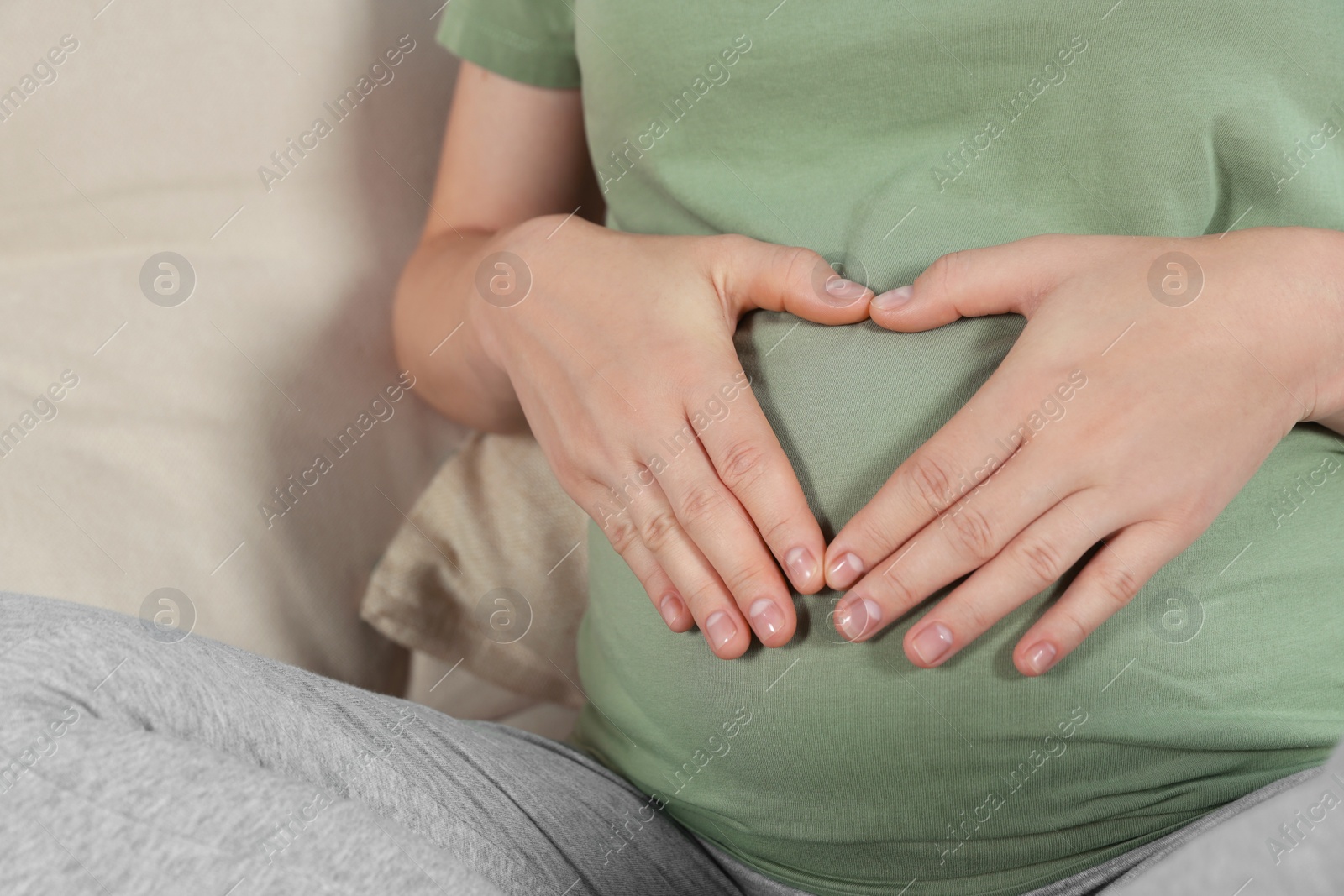 Photo of Pregnant woman making heart with her hands on sofa, closeup