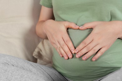 Photo of Pregnant woman making heart with her hands on sofa, closeup