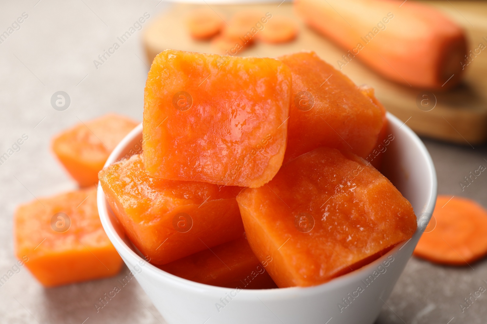 Photo of Bowl of frozen carrot puree cubes and ingredient on marble table, closeup