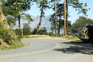 Empty asphalted road near mountains and trees outdoors