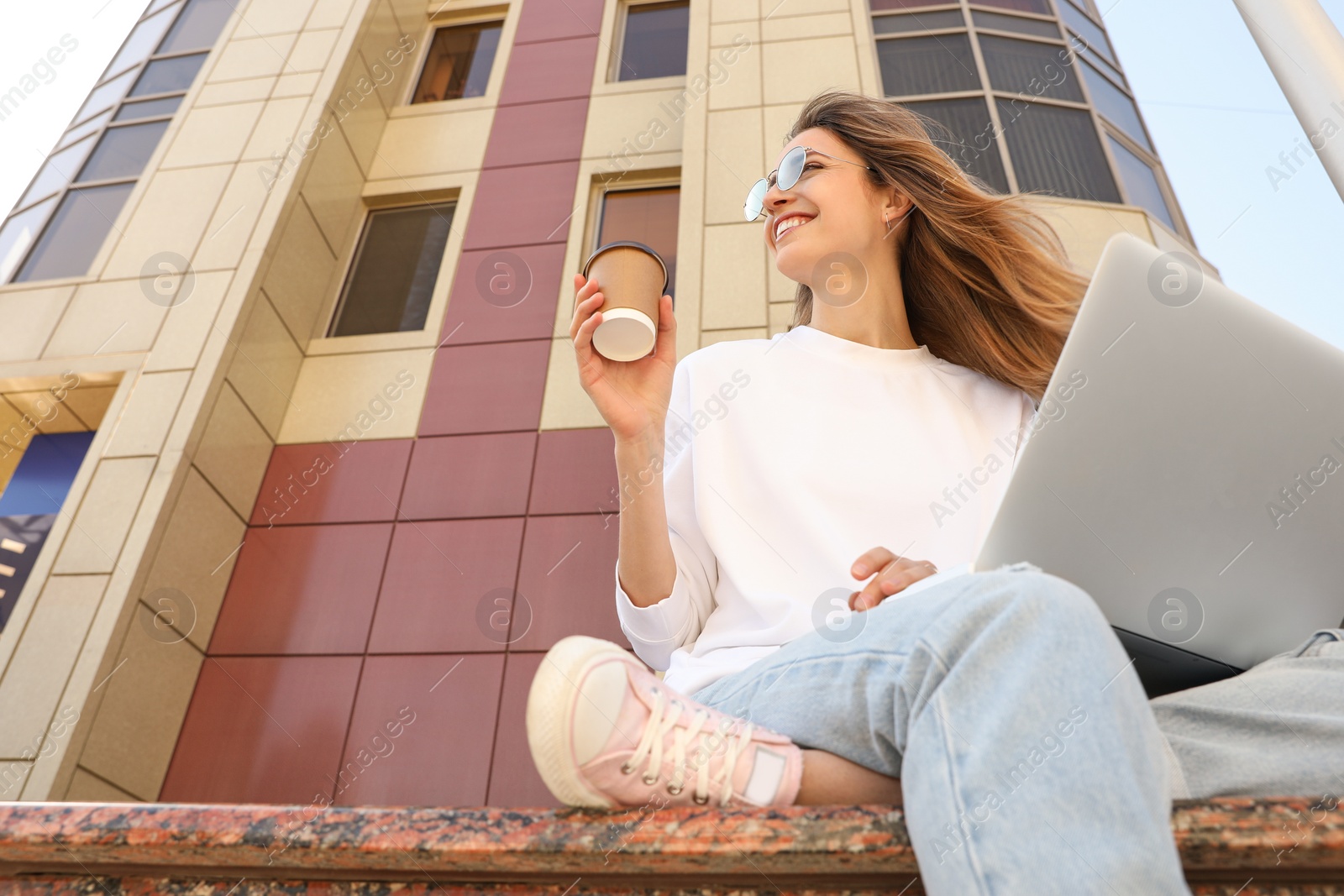 Image of Young woman with paper cup of coffee and laptop outdoors