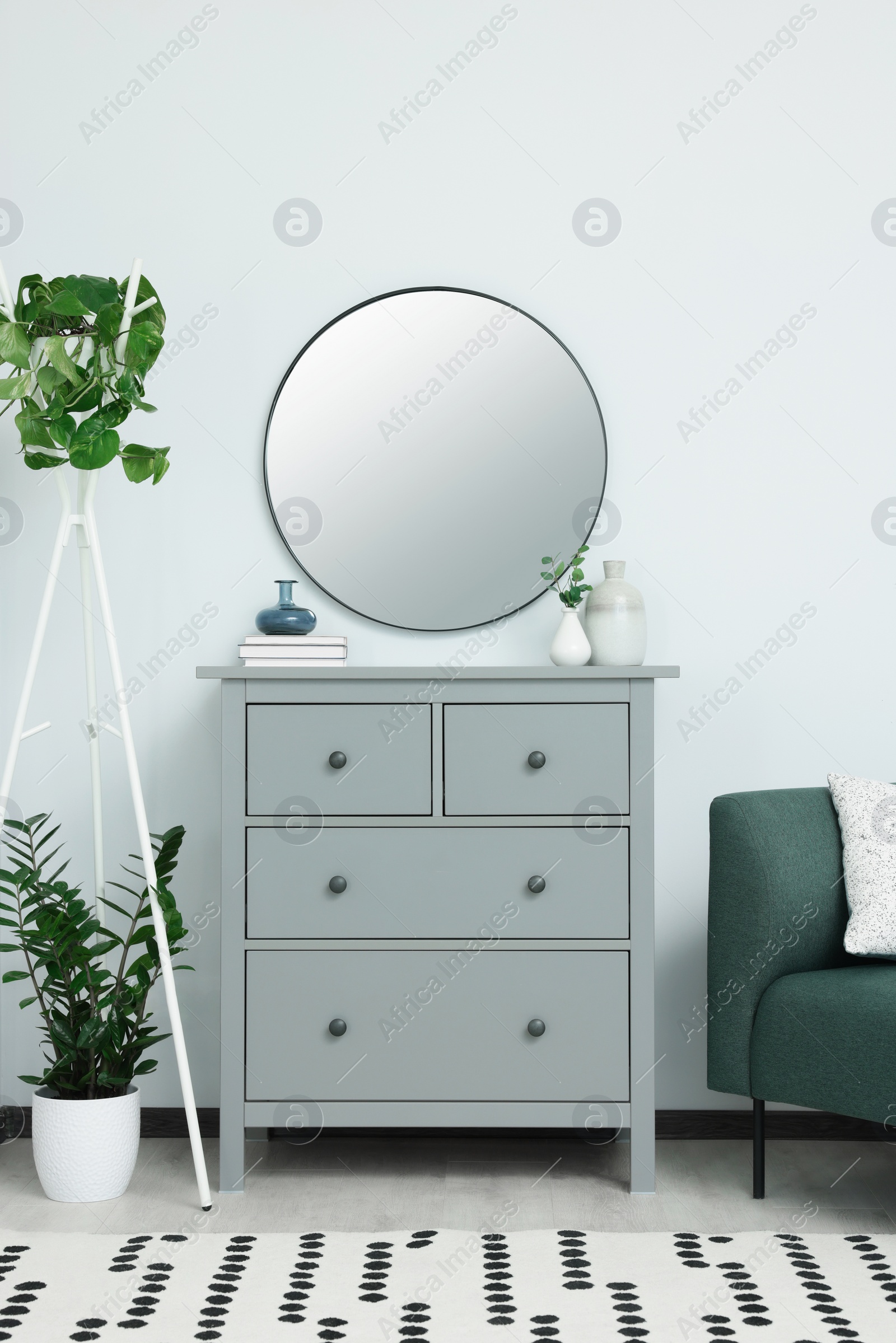 Photo of Chest of drawers and stylish round mirror on white wall indoors. Interior design