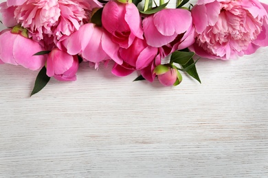 Photo of Fragrant peonies on wooden table, top view with space for text. Beautiful spring flowers