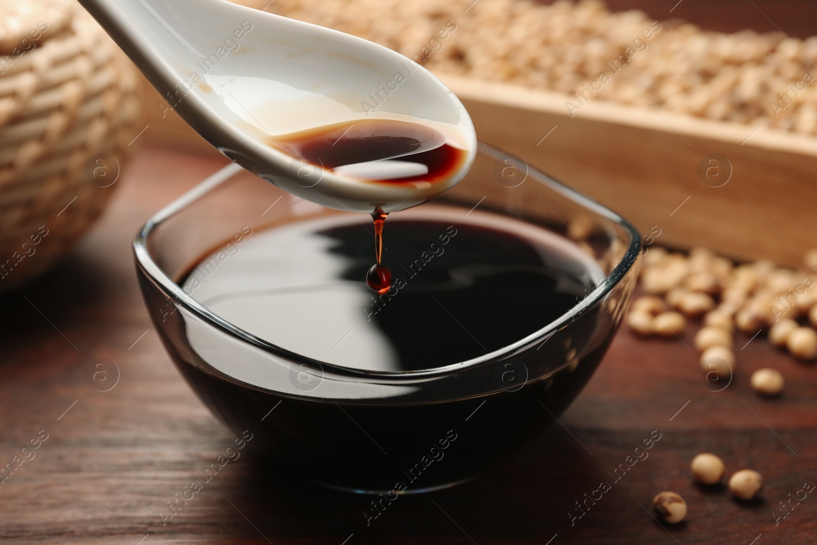 Photo of Taking soy sauce with spoon from bowl at wooden table, closeup