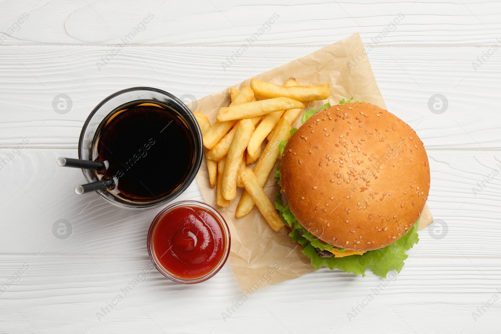Photo of French fries, tasty burger, sauce and drink on white wooden table, flat lay