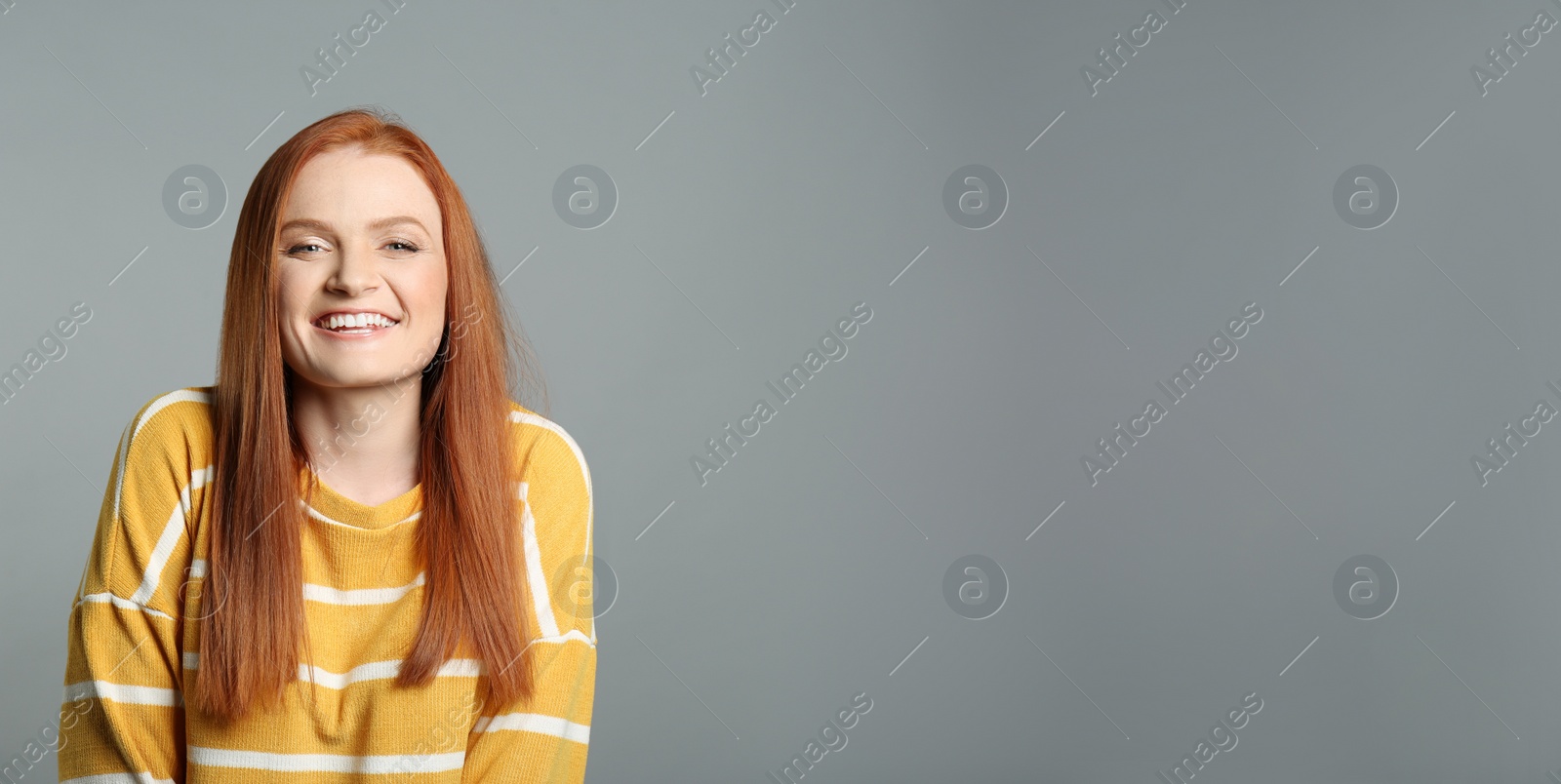 Photo of Candid portrait of happy young woman with charming smile and gorgeous red hair on grey background, space for text