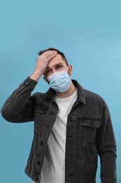 Man in mask suffering from headache on light blue background. Cold symptoms