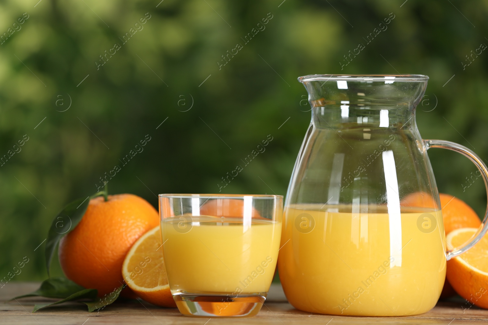 Photo of Delicious orange juice and fresh fruits on wooden table against blurred background