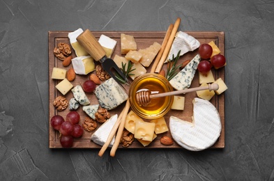 Cheese plate with honey, grapes and nuts on grey table, top view