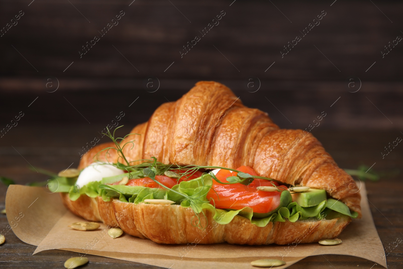 Photo of Tasty croissant with salmon, avocado, mozzarella and lettuce on wooden table, closeup