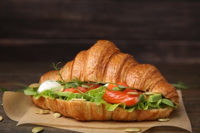 Photo of Tasty croissant with salmon, avocado, mozzarella and lettuce on wooden table, closeup