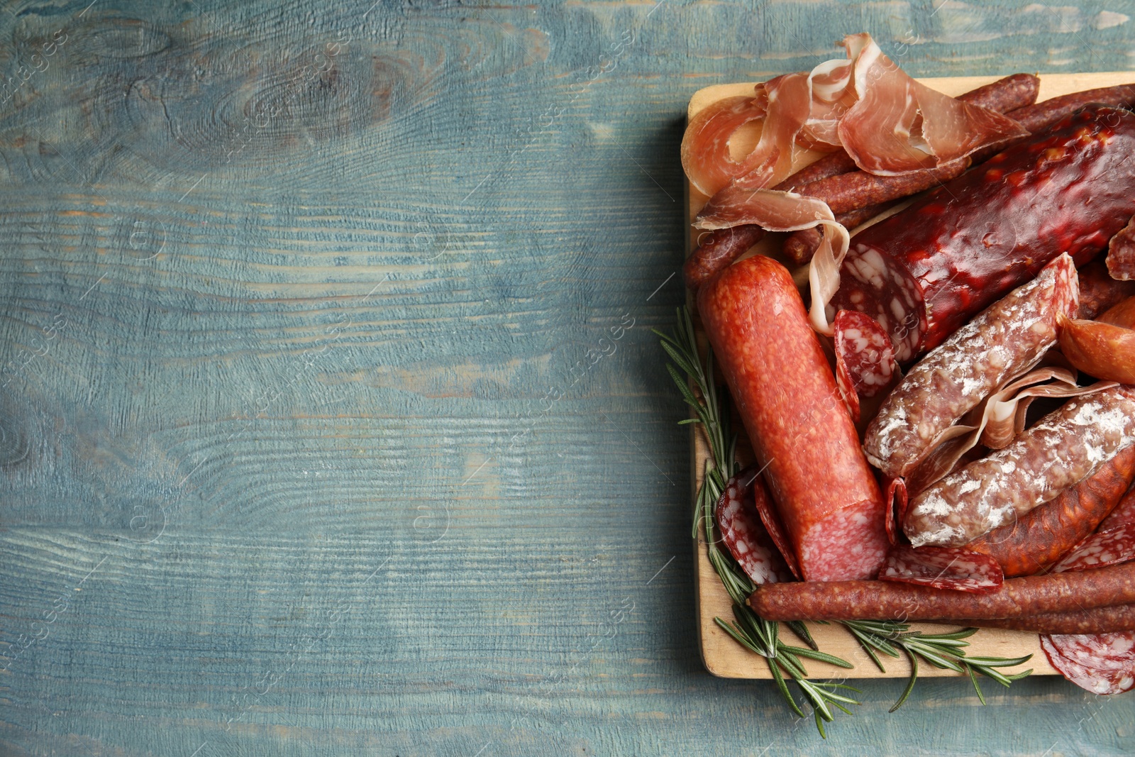 Photo of Different types of sausages served on light blue wooden table, top view. Space for text