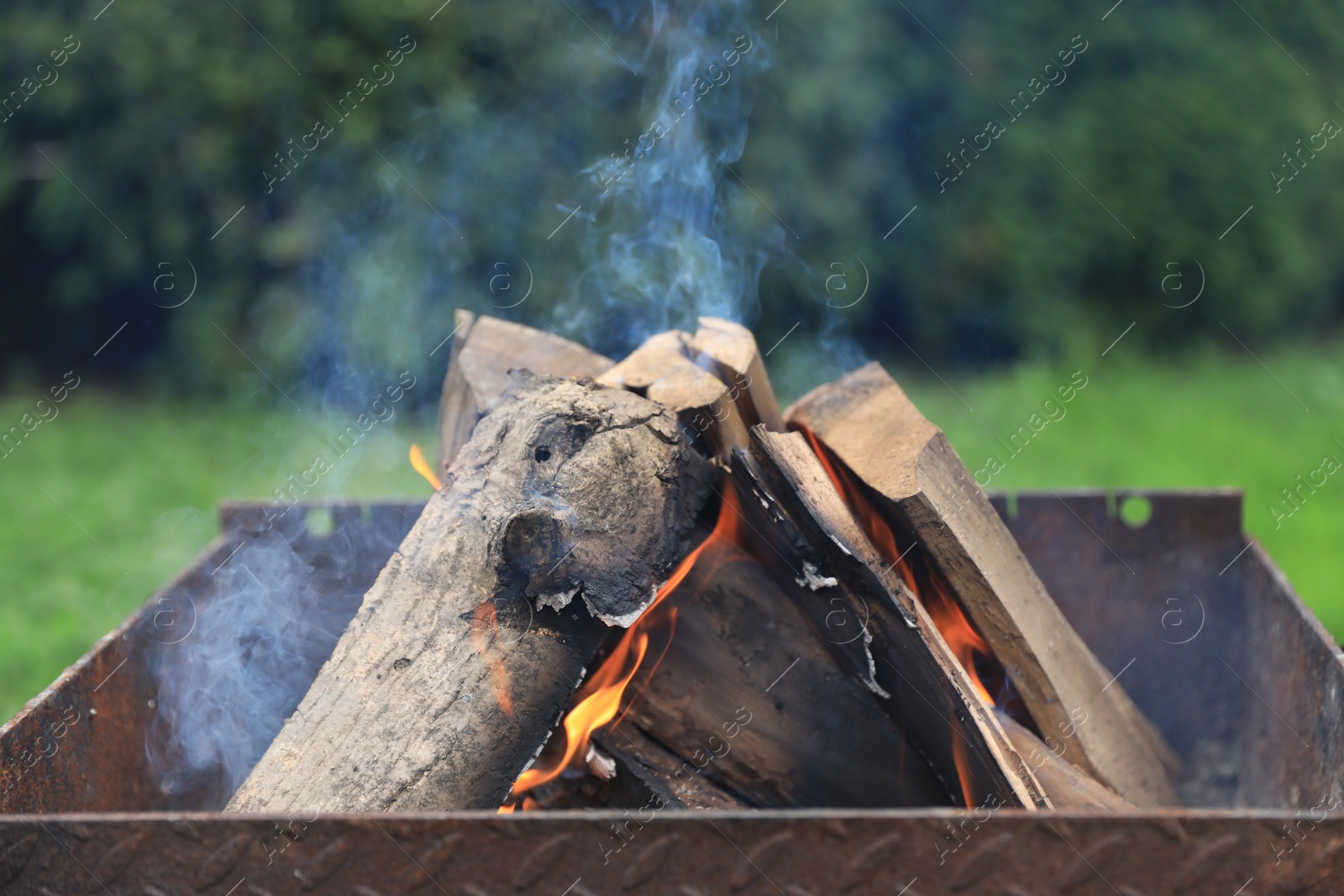 Photo of Metal brazier with burning firewood outdoors, closeup