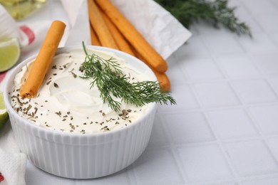 Delicious cream cheese with grissini stick and dill on white tiled table, closeup. Space for text