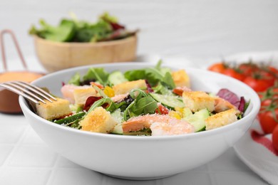 Photo of Delicious salad with croutons, cucumber and shrimp served on white tiled table, closeup