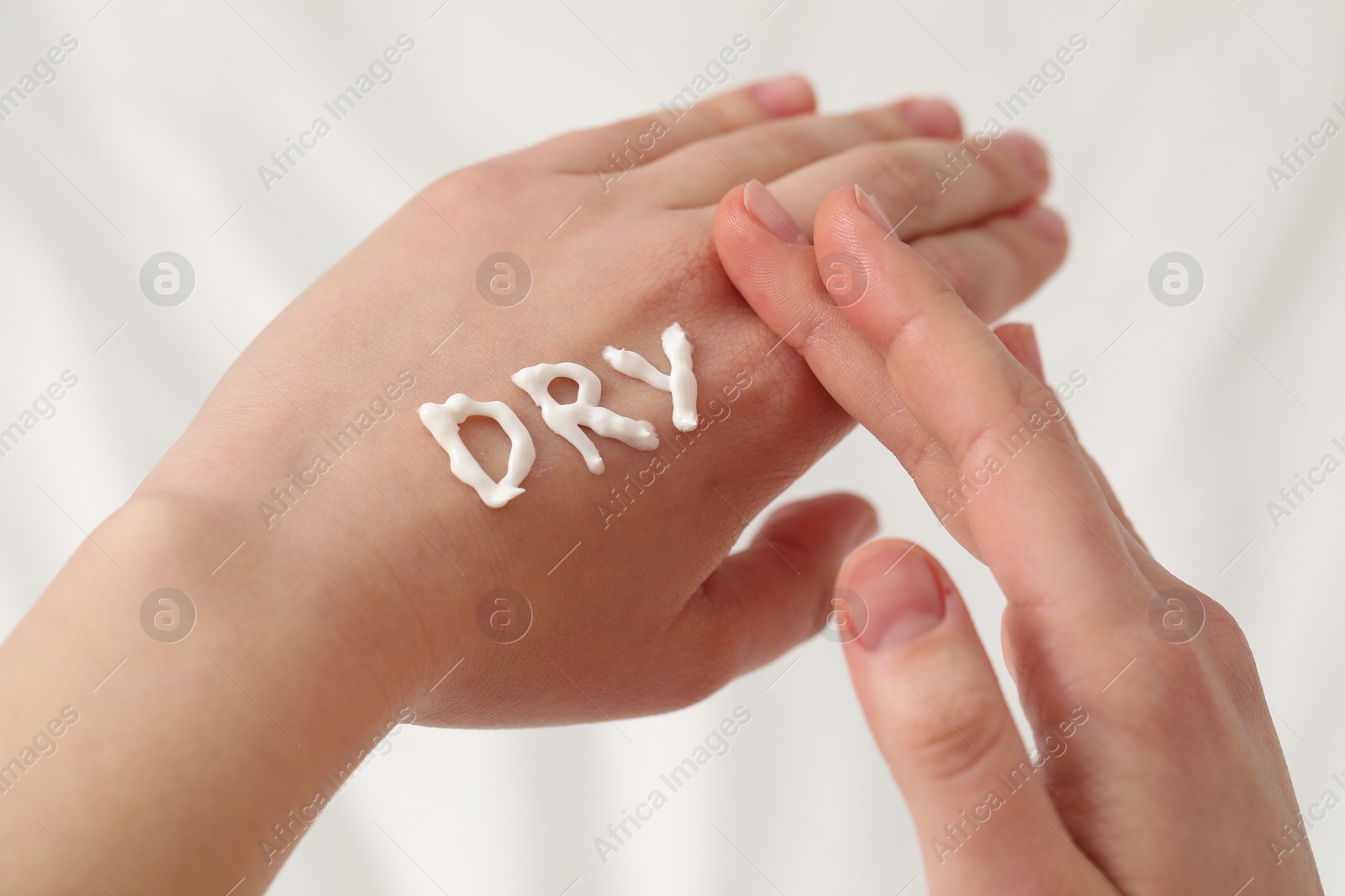 Photo of Young woman with word Dry made of cream on her hand on bed, closeup