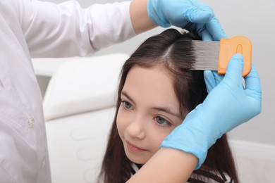 Photo of Doctor using nit comb on little girl's hair indoors. Anti lice treatment