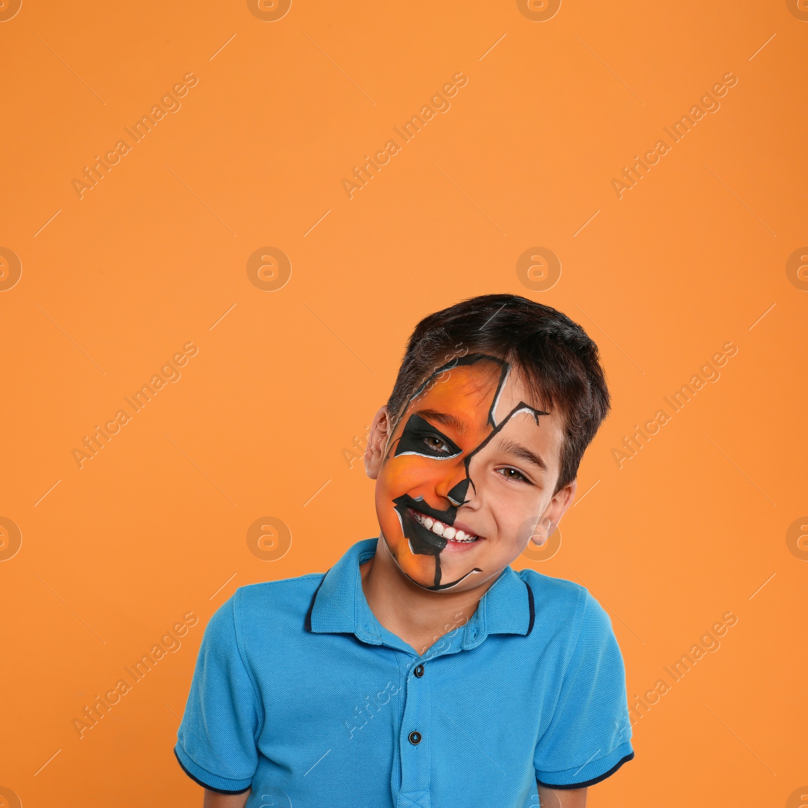 Photo of Cute little boy with face painting on orange background