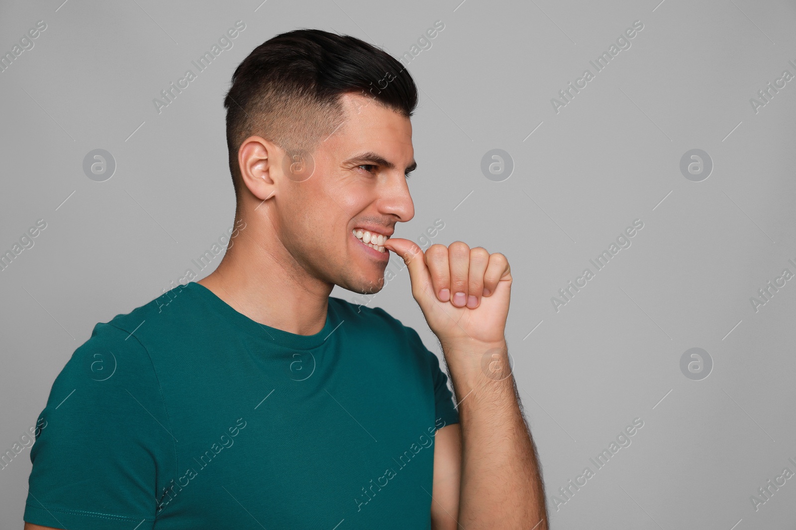 Photo of Man biting his nails on grey background. Bad habit