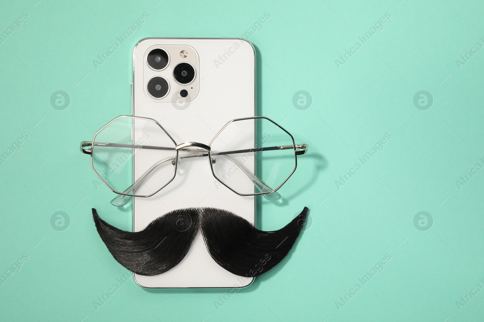 Photo of Artificial moustache, smartphone and glasses on turquoise background, top view. Space for text