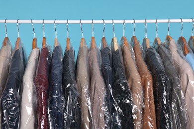 Photo of Dry-cleaning service. Many different clothes in plastic bags hanging on rack against light blue background