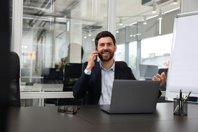 Photo of Man with laptop talking on phone at black desk in office
