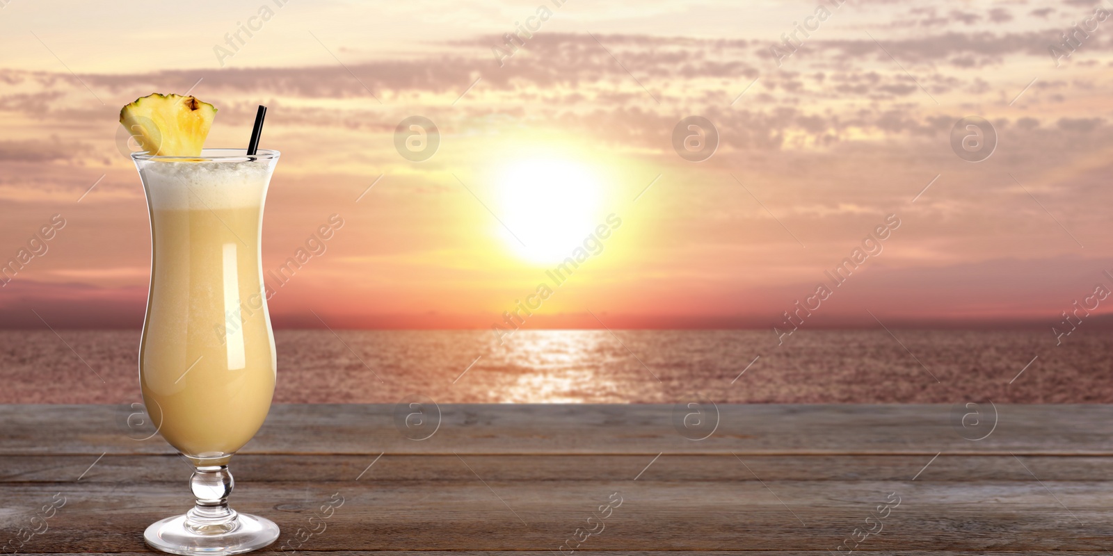 Image of Tasty Pina Colada cocktail on wooden table near ocean at sunset, space for text. Banner design